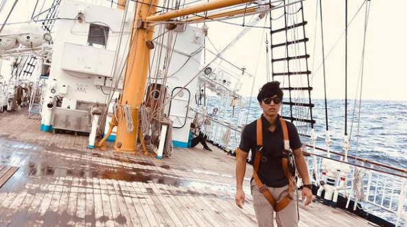 A dark haired sailor walking on the deck of a moving ship. 