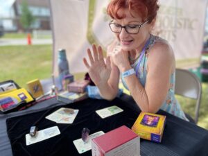 A middle-aged woman wearing glasses talks with her hands while interpreting cards spread out on a black cloth in front of her.